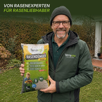 Ein lächelnder Mann mit Brille und grüner Jacke steht auf einem Rasen und hält eine Tüte „TerraUno Premium – Herbst-Rasendünger“ in der Hand. Der Text darüber lautet: Von Rasenexperten für Rasenliebhaber – so können Sie Ihren Rasen optimal auf den Winter vorbereiten.