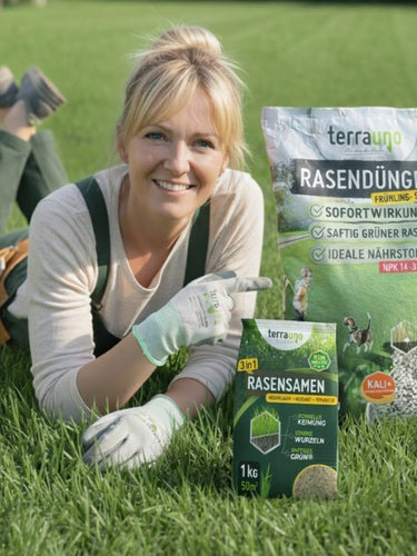 Eine lächelnde Frau in Gartenhandschuhen und Latzhose liegt auf grünem Gras, hält eine Tüte mit Grassamen in der Hand und zeigt auf eine große Tüte Rasendünger mit deutscher Aufschrift.