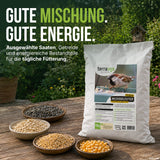 Auf einem Tisch im Freien steht eine Tüte „TerraUno Premium Wildvogelfutter“, umgeben von Schalen, die mit Samen und Körnern gefüllt sind. Auf der Verpackung ist ein Vogel abgebildet, und ein deutscher Text beschreibt dieses nahrhafte, schalenlose Vogelfutter als ideales Ganzjahresfutter für Wildvögel. Im Hintergrund bildet üppiges Grün eine natürliche Kulisse.