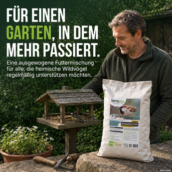 Ein Mann steht in einem Garten neben einem Vogelfutterhäuschen und hält eine Tüte „TerraUno Premium Wildvogelfutter“ in der Hand. Der Text ruft dazu auf, Wildvögel mit dieser ausgewogenen Futtermischung zu unterstützen, die ihnen das ganze Jahr über die nötige Nahrung liefert.